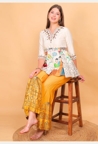Woman sitting on a wooden stool wearing a patterned top and yellow pants against a beige background