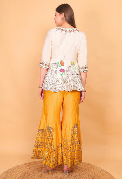 Woman wearing a white embroidered top and yellow patterned pants on a beige background