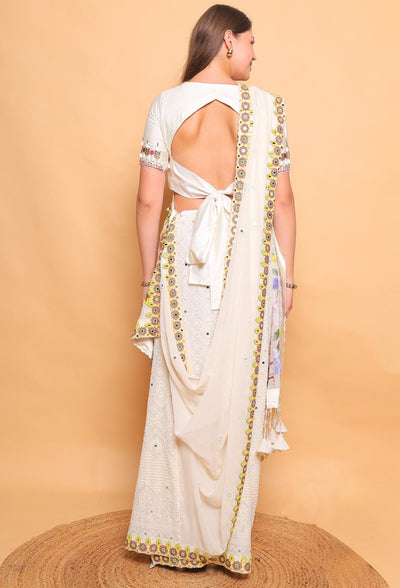 Woman wearing a white saree with gold embroidery against a beige background